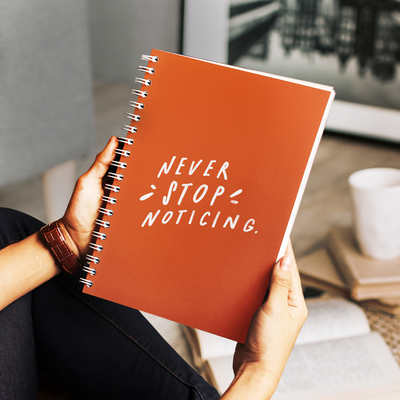 Bright orange 6” x 8” spiral notebook with hand-lettered quote about mindfulness on the cover.