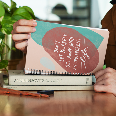 Motivating quote about living your best life hand-lettered and illustrated with abstract shapes on a spiral A5 notebook. 