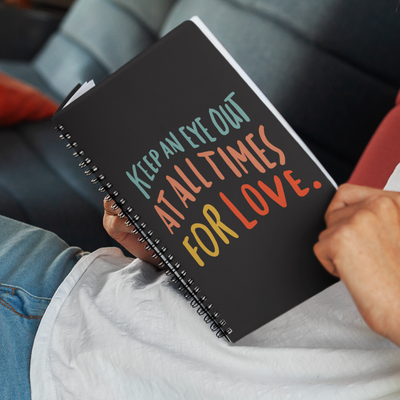 Inspiring quote about love printed in colorful big lettering on a black spiral A5 notebook. 