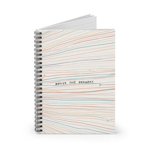 Spiral notebook, standing up on table, showing the cover with colourful lines and quote about mindfulness. 