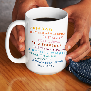 Close-up of hands holding a large white coffee mug with an inspiring poem about creativity printed on the side.