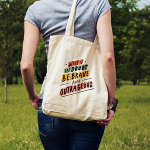 Woman in a field carrying her tote bag over her shoulder. Bag has an inspiring quote about being your best self