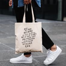 Load image into Gallery viewer, Man from waist down in casual outfit, holding a canvas tote bag with big black quote about following your dreams
