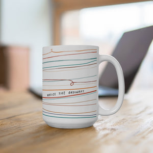 15-ounce beautiful coffee mug on a desk. Mug is designed with whimsical colorful lines and a quote that reads “Notice the Ordinary.”