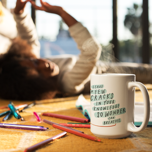 Creative scene of person laying happily on carpet behind coffee mug and colored pencils. The mug features an inspiring quote. 