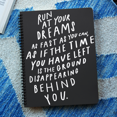 Black and white 6” x 8” spiral notebook with hand-lettered and illustrated quote about following your dreams on the cover.