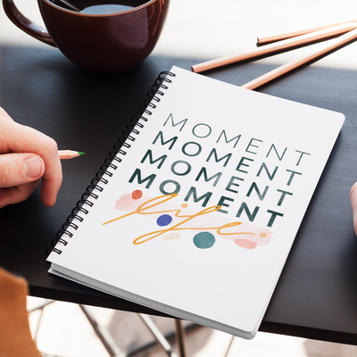 Inspiring statement about cherishing the little moments, with cute abstract shapes, printed on the cover of a spiral notebook. 