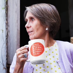 Older woman in her 70s, profile view, holding a beautiful white 15 ounce coffee mug that has a feel-good quote about aging.