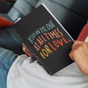 Man reclining with open spiral journal on his lap. Journal cover is black with quote about love in colourful lettering.