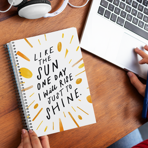 Woman hands holding a spiral journal with creatively hand-lettered quote about living your best life, on desk with laptop.